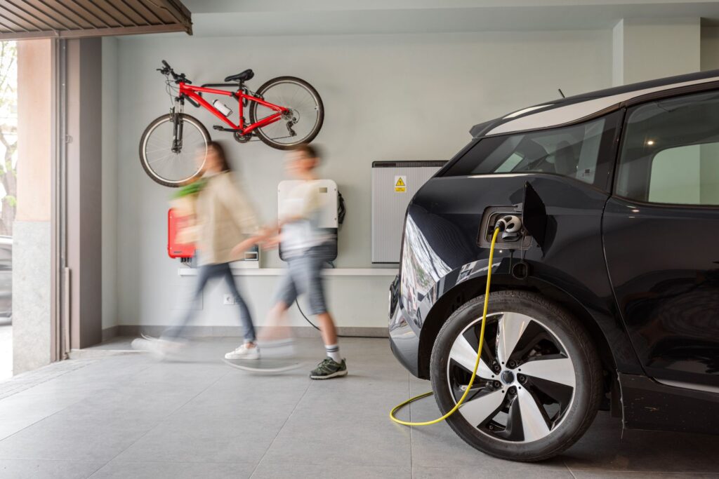 Electric vehicle charging in a modern home garage with a family walking by.  