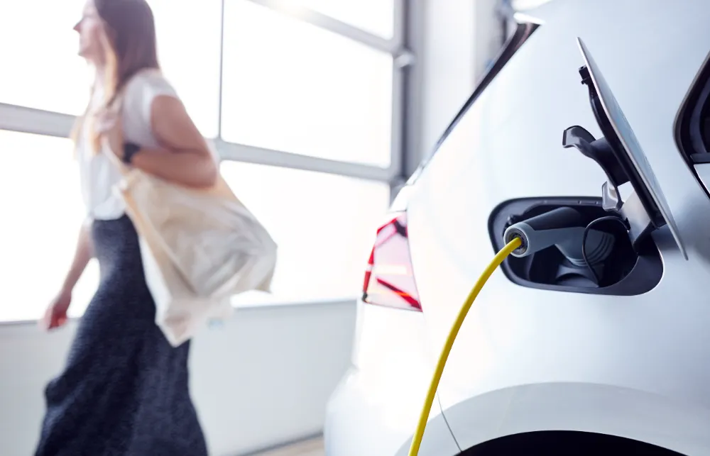 Close-up of an electric vehicle charging with a yellow cable as a woman walks by in a modern Sparks NV garage