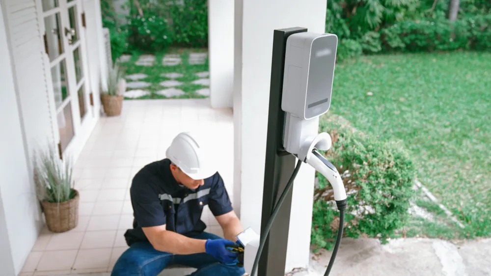 Sparks NV EV charger installation — technician in a hard hat kneeling beside a wall-mounted home charging station, inspecting wiring and equipment on a residential patio.